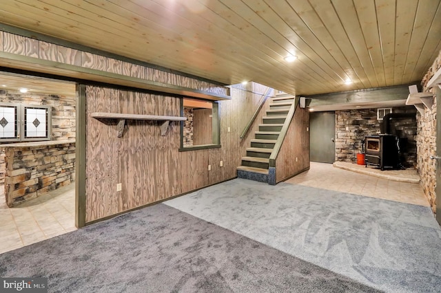 basement featuring wood walls, light colored carpet, a wood stove, and wooden ceiling