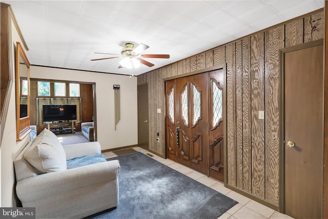 tiled foyer entrance featuring wood walls, ceiling fan, and ornamental molding