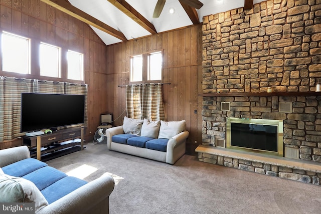 living room with ceiling fan, beam ceiling, carpet, and a stone fireplace