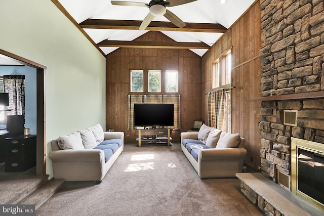 carpeted living room featuring wooden walls, beam ceiling, ceiling fan, and a stone fireplace