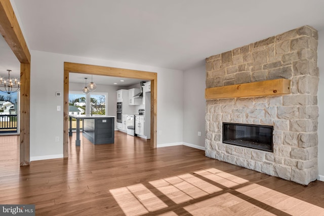 unfurnished living room with a chandelier, a stone fireplace, baseboards, and wood finished floors