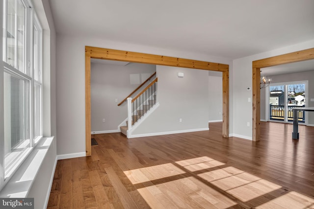 spare room with stairway, an inviting chandelier, baseboards, and wood finished floors