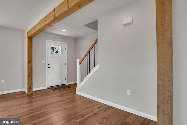 foyer entrance with beamed ceiling, stairs, baseboards, and wood finished floors