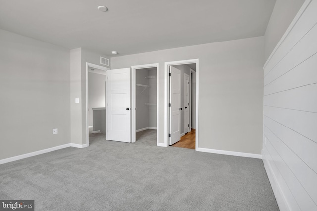 unfurnished bedroom with visible vents, a walk in closet, baseboards, carpet floors, and a closet