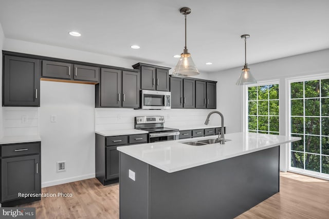 kitchen featuring a center island with sink, stainless steel appliances, pendant lighting, sink, and light hardwood / wood-style floors