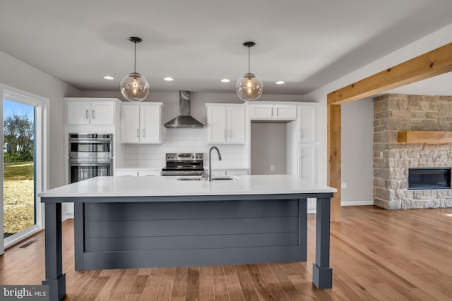 kitchen featuring a sink, a stone fireplace, appliances with stainless steel finishes, wall chimney exhaust hood, and light countertops