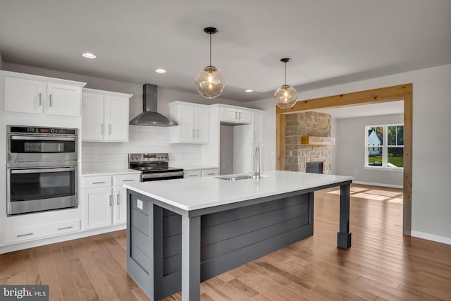 kitchen with a sink, wall chimney range hood, stainless steel appliances, light wood finished floors, and light countertops