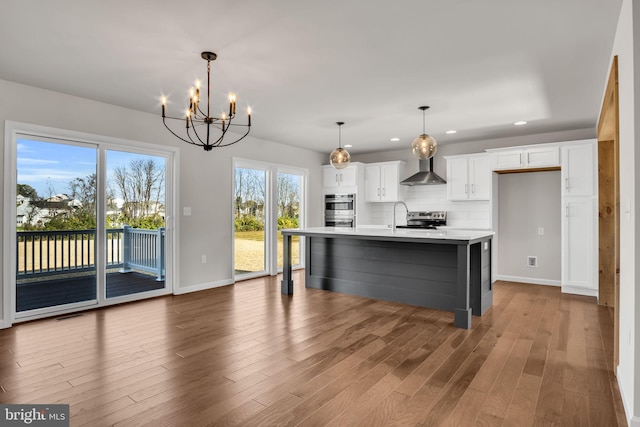 kitchen with tasteful backsplash, wood finished floors, stainless steel appliances, wall chimney exhaust hood, and light countertops