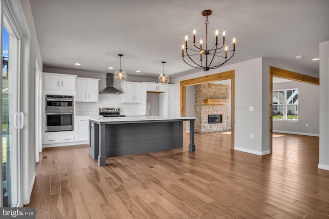 kitchen with a stone fireplace, white cabinets, appliances with stainless steel finishes, wall chimney exhaust hood, and tasteful backsplash