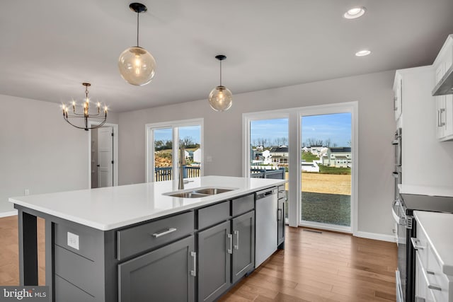 kitchen featuring wood finished floors, a center island with sink, gray cabinets, a sink, and appliances with stainless steel finishes