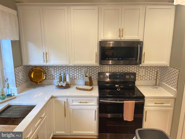 kitchen featuring decorative backsplash, stainless steel microwave, white cabinets, and black / electric stove