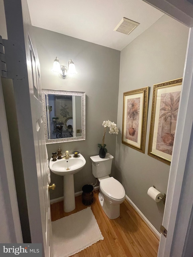 half bathroom featuring wood finished floors, visible vents, baseboards, a sink, and toilet