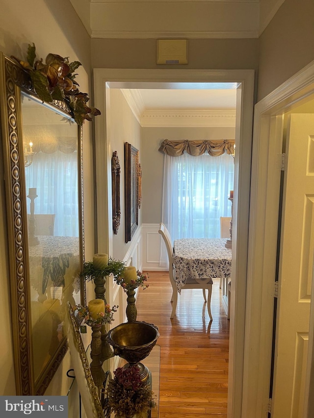 corridor featuring visible vents, ornamental molding, light wood-style floors, wainscoting, and a decorative wall