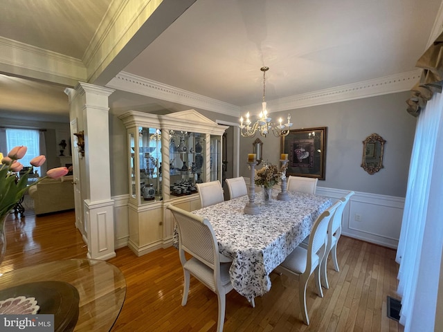 dining area featuring ornamental molding, an inviting chandelier, wood-type flooring, and ornate columns