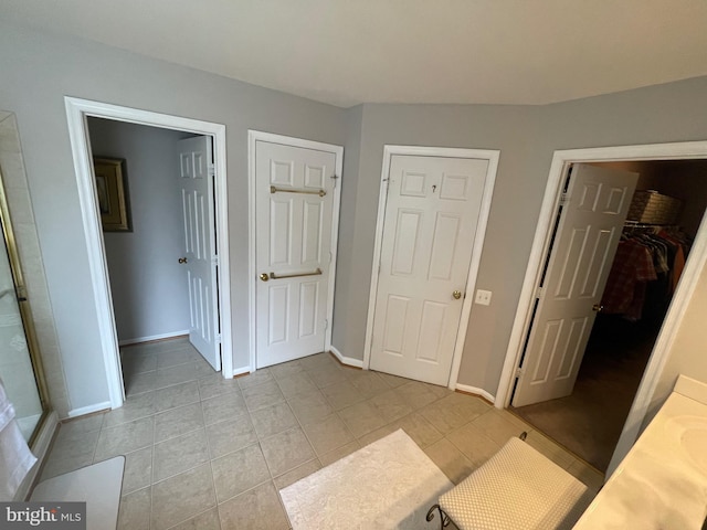 bedroom with a walk in closet, light tile patterned floors, baseboards, and a closet