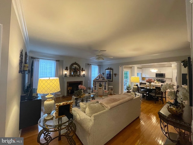 living area with hardwood / wood-style floors, ornate columns, a fireplace, ceiling fan, and crown molding