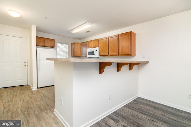 kitchen featuring a breakfast bar, kitchen peninsula, hardwood / wood-style floors, and white appliances