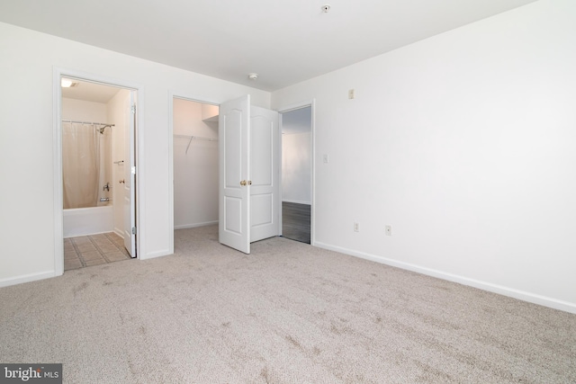 unfurnished bedroom with ensuite bath, a walk in closet, light colored carpet, and a closet