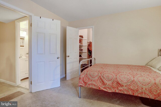 carpeted bedroom with a walk in closet, vaulted ceiling, and ensuite bath