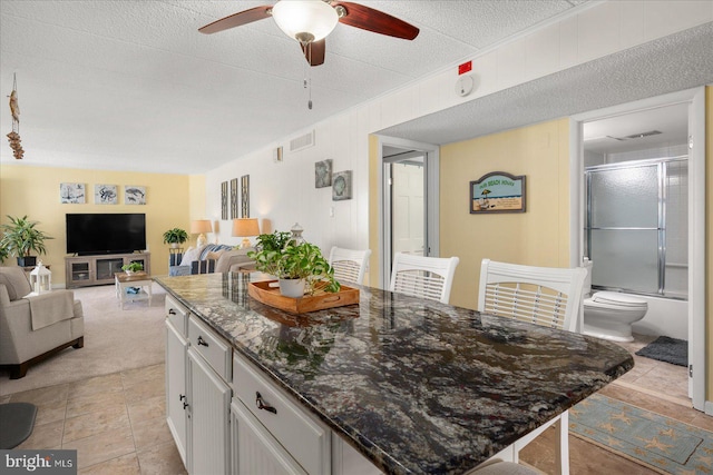 kitchen with dark stone countertops, light tile patterned floors, a kitchen island, ceiling fan, and white cabinets