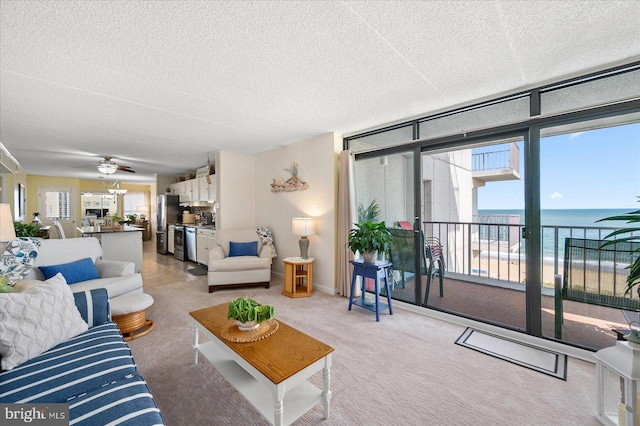 living room featuring a water view, ceiling fan, a wealth of natural light, and a textured ceiling