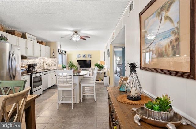 kitchen featuring white cabinetry, light tile patterned floors, stainless steel appliances, ceiling fan, and a breakfast bar area