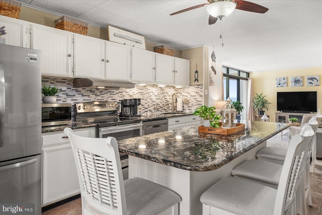 kitchen featuring ceiling fan, stainless steel appliances, white cabinetry, and a breakfast bar