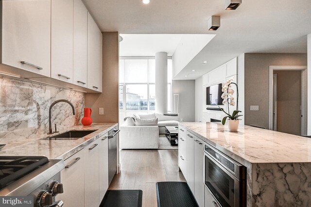 kitchen with appliances with stainless steel finishes, white cabinetry, tasteful backsplash, light hardwood / wood-style flooring, and sink