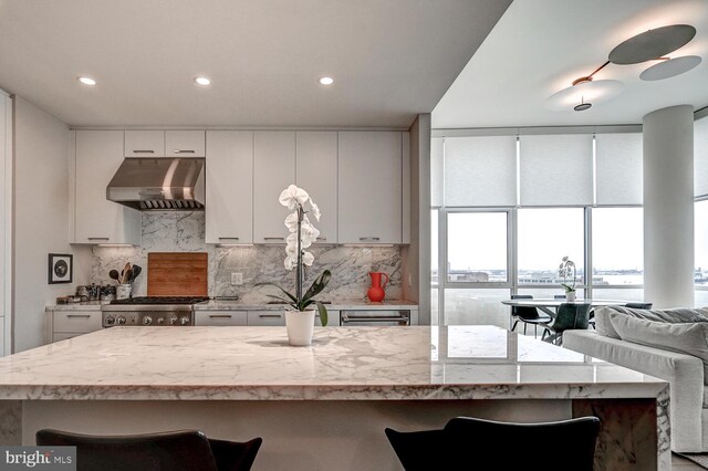 kitchen featuring light stone counters, stainless steel range oven, white cabinetry, backsplash, and exhaust hood