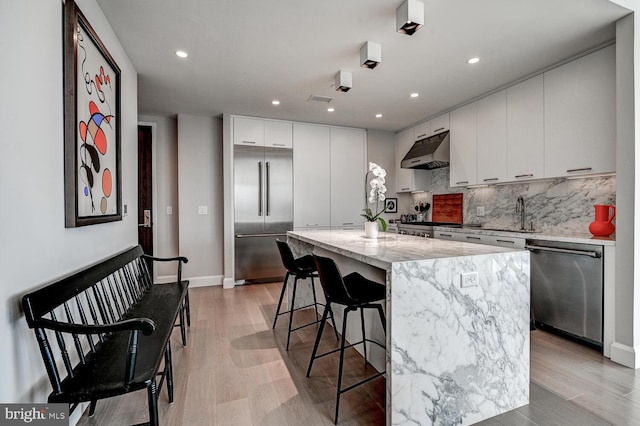 kitchen featuring white cabinets, light hardwood / wood-style flooring, appliances with stainless steel finishes, a center island, and decorative backsplash