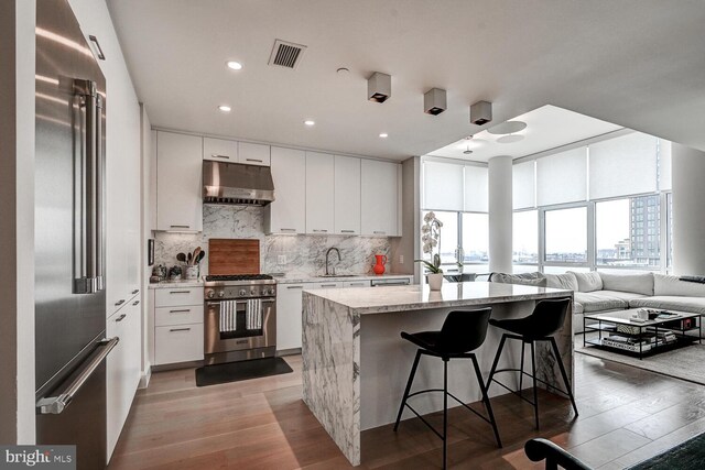 kitchen with white cabinets, light hardwood / wood-style floors, high end appliances, a center island with sink, and a kitchen bar