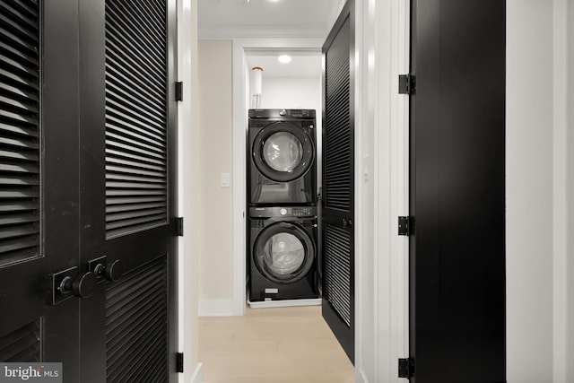 clothes washing area with stacked washing maching and dryer, light hardwood / wood-style floors, and crown molding