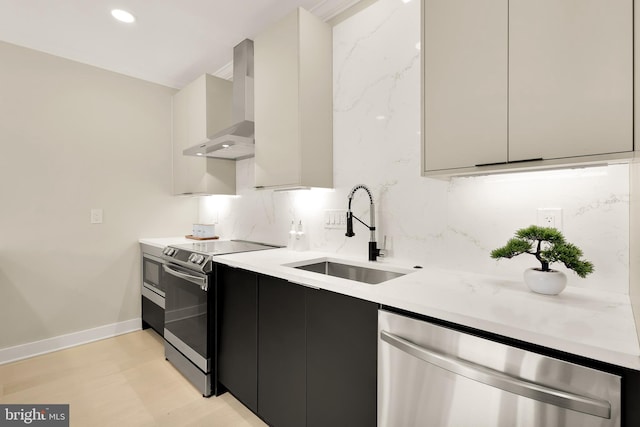 kitchen featuring tasteful backsplash, stainless steel appliances, light stone counters, sink, and wall chimney range hood