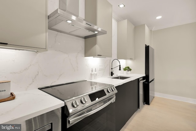 kitchen featuring light hardwood / wood-style flooring, light stone counters, stainless steel appliances, sink, and wall chimney range hood