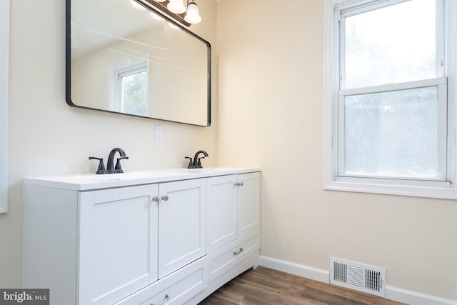 bathroom featuring visible vents, a sink, wood finished floors, double vanity, and baseboards