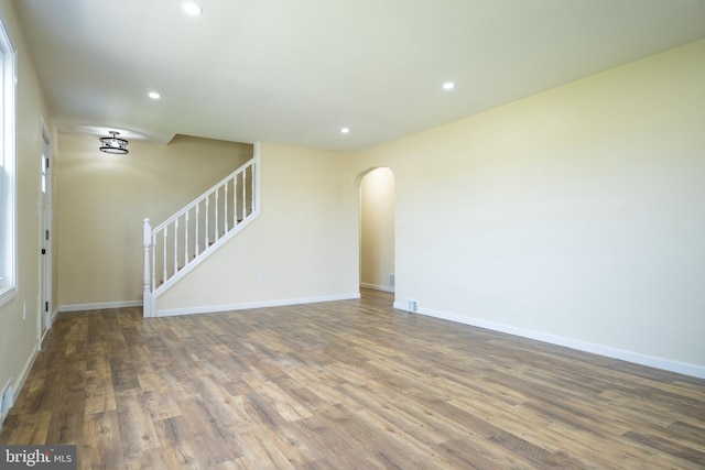 unfurnished living room featuring wood finished floors, baseboards, recessed lighting, arched walkways, and stairs