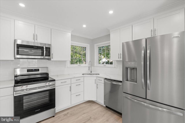 kitchen with tasteful backsplash, crown molding, appliances with stainless steel finishes, white cabinetry, and a sink