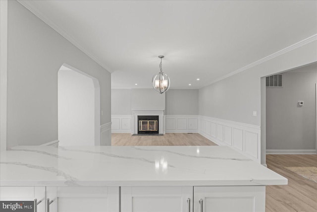 kitchen with light wood-type flooring, visible vents, a fireplace with flush hearth, white cabinets, and light stone countertops