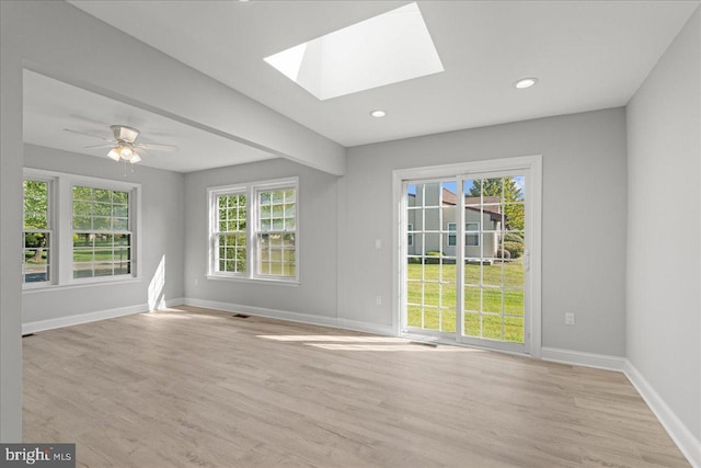 spare room featuring a skylight, a healthy amount of sunlight, baseboards, and light wood-style flooring