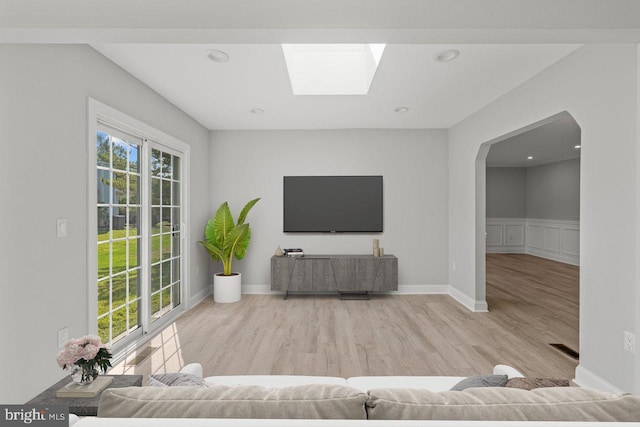 unfurnished living room with a wainscoted wall, wood finished floors, arched walkways, a skylight, and a decorative wall