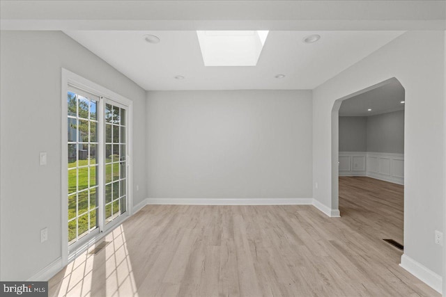 empty room featuring wainscoting, visible vents, light wood-style flooring, and a skylight