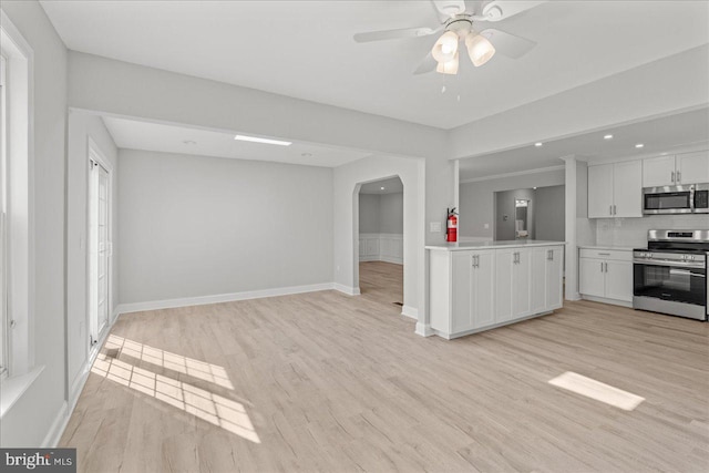 kitchen featuring light countertops, light wood-style flooring, arched walkways, and appliances with stainless steel finishes