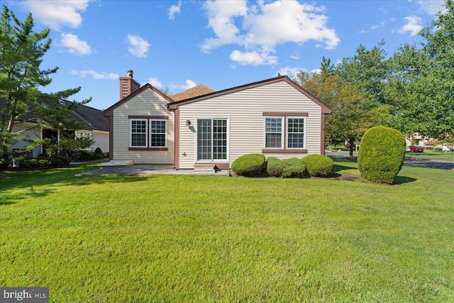 back of property with entry steps, a yard, a patio area, and a chimney