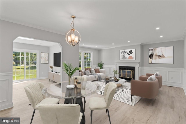 dining space featuring a glass covered fireplace, recessed lighting, light wood-style floors, crown molding, and a decorative wall