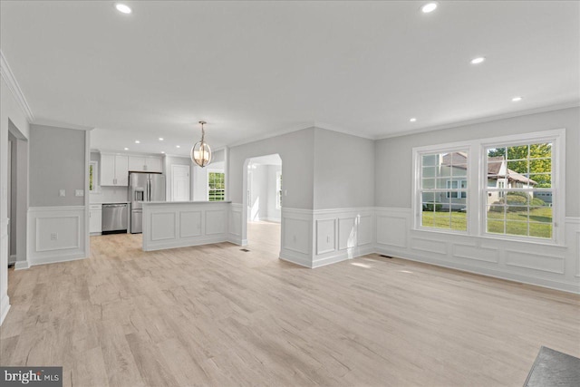 unfurnished living room with arched walkways, plenty of natural light, recessed lighting, and light wood finished floors