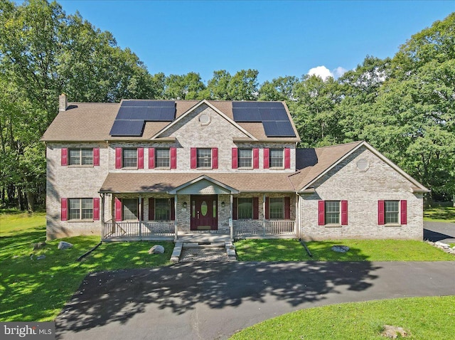 colonial house featuring a porch, a front lawn, and solar panels