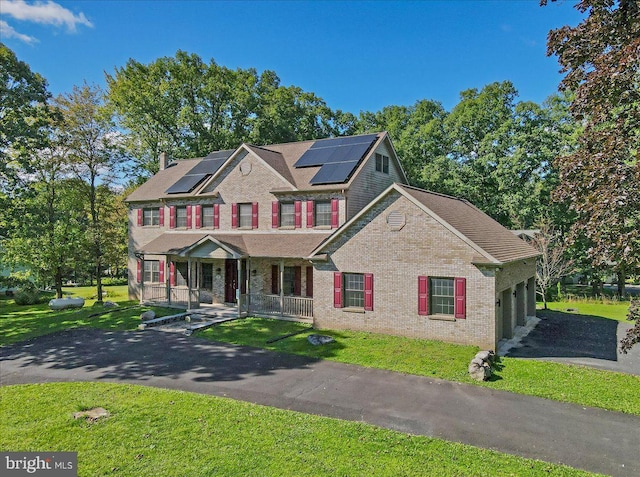 view of front of home featuring solar panels, covered porch, and a front lawn