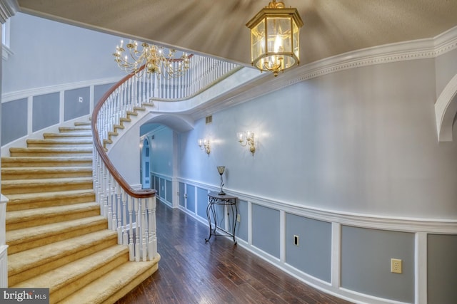 stairs with a textured ceiling, a notable chandelier, ornamental molding, hardwood / wood-style flooring, and a towering ceiling