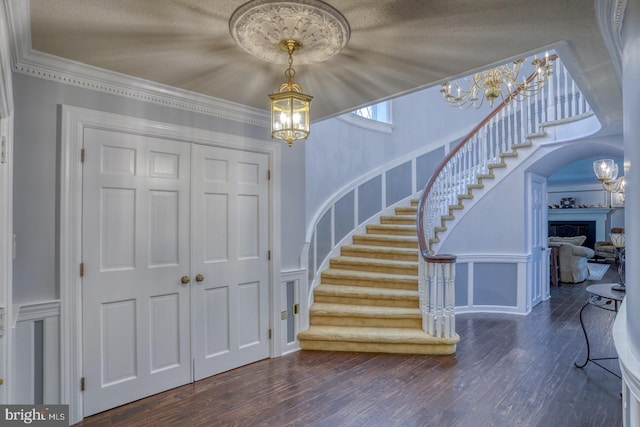 entryway with dark wood-type flooring, ornamental molding, and an inviting chandelier