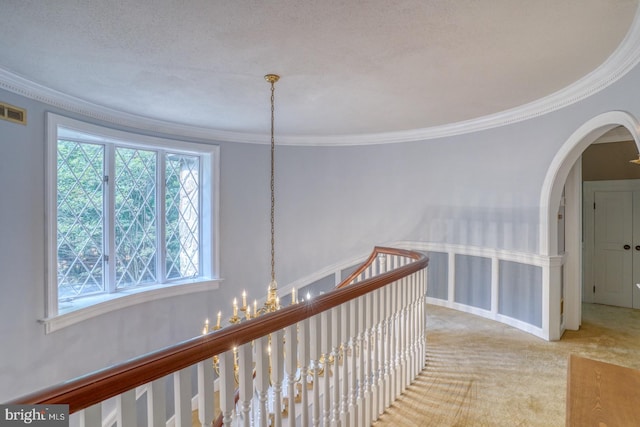 hall with a textured ceiling, crown molding, a notable chandelier, and carpet floors